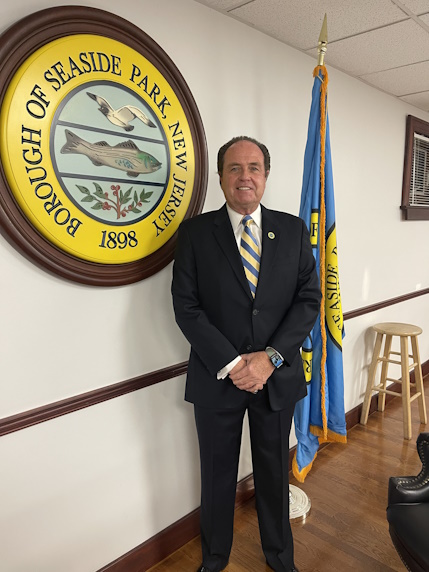 Council Member Connor standing in front of the American Flag and the Borough Seal